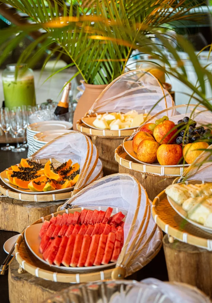 Cestos de fibra natural com frutas tropicais frescas — melancia, mamão e uvas — servidos no café da manhã do Campo Bahia Hotel Villas Spa